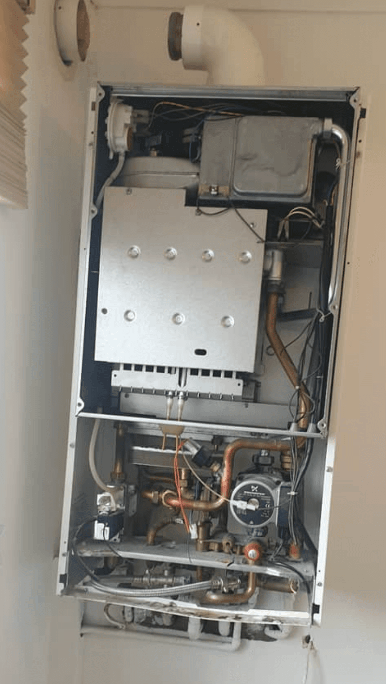 Older wall-mounted boiler with the case off — exposed heat exchanger and pipework before replacement