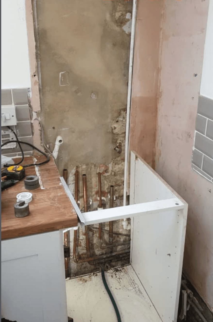 Kitchen with the old boiler removed — exposed wall, capped pipework, base unit pulled forward